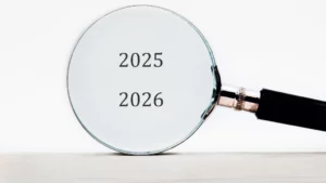 Eine Lupe vergrößert die Zahlen 2025 und 2026 vor einem einfarbigen Hintergrund. Der Fokus liegt auf den nächsten beiden Jahren, was auf eine Planung hindeutet.